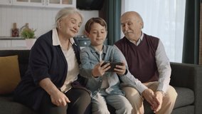 Little boy visiting his grandparents. Happy elderly couple sitting on sofa and chatting with their little grandchild. They are taking selfies together. - Powered by Shutterstock - Get 15% off with code: PIKWIZARD15