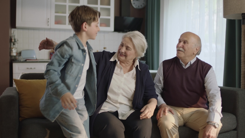 Little boy visiting his grandparents. Happy elderly couple sitting on sofa and chatting with their little grandchild. Happy family portrait with grandchildren. Royalty-Free Stock Footage #1090511869