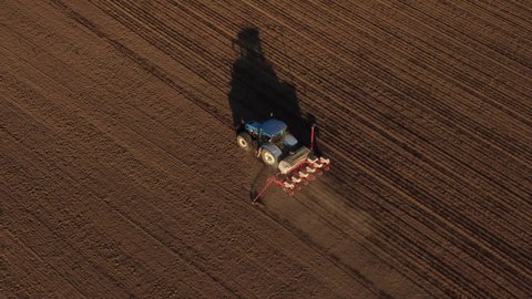 Aerial view of tractor at work in spring field. Time of sowing. Shooting from drone flying over tractor in field with prepared soil for planting, new harvest. Agriculture concept. Rural landscape.