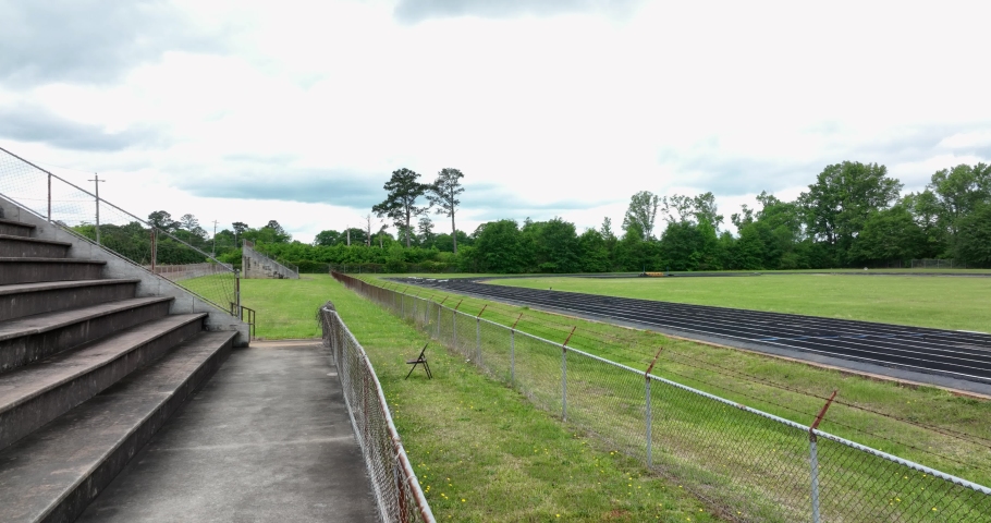 A quarter mile running track with concrete stadium seating and chain link fencing under a bright sky
