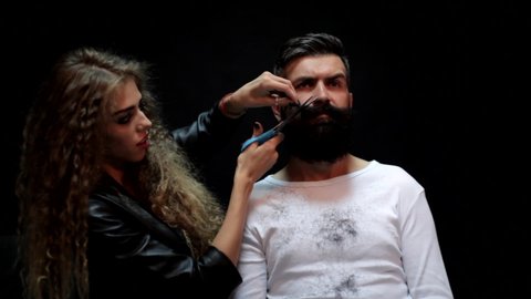 Barbershop or hairdresser. Sexy woman hairdresser cuts beard with scissors. Female barber. Man with long beard, mustache and stylish hair.