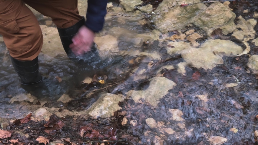 Man rubber boots river. Washes boots in cold water. Spring hike in the forest. High khaki fishing boots. The concept of rural life, hiking. travel, outdoor recreation. Walking on a mountain river