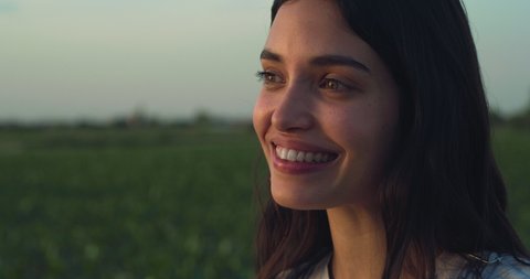 Cinematic shot of young female farmer is enjoying nature around and smiling satisfied with her work on countryside farm corn fields at sunset.
