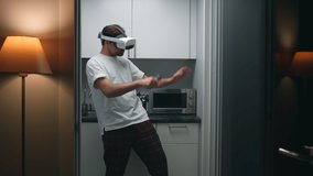 Funny man in pajamas dance in kitchen in augmented reality headset. Guy in vr goggles dancing at home