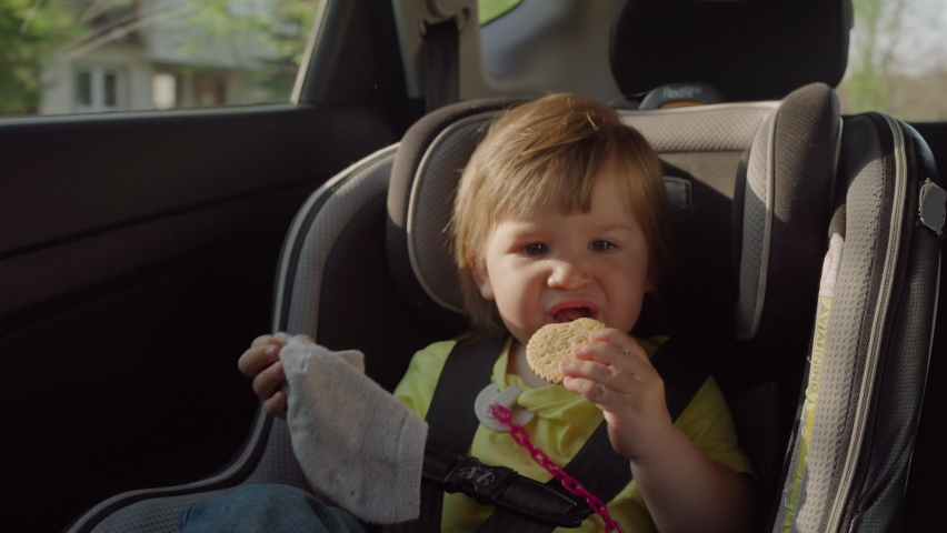 The child eats cookies while traveling in the car. A child sits in a child car seat during a road trip.