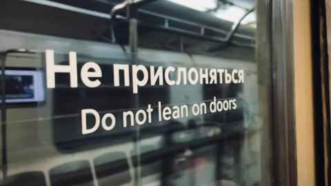 Text on the door "Do Not Lean On Doors" in Russian and English. Riding Subway Train in 4K Slow motion. Subway sign for passengers. Warning Do Not Lean on Subway Door. Safety on public transport.
