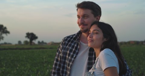 Cinematic authentic shot of carefree happy romantic couple of farmers is enjoying sunset together and hugging with affection as sign of timeless love on farmland corn fields.