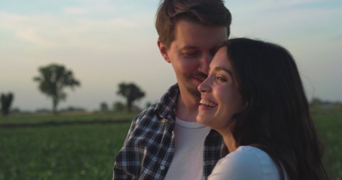Cinematic authentic shot of carefree happy romantic couple of farmers is enjoying sunset together and hugging with affection as sign of timeless love on farmland corn fields.