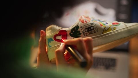 Black Female Designer Putting Coloured Unique Patterns on Sneakers During the Evening in Creative Environment. Girl Drawing on the Shoes. Fashion and Modern Occupation Concept