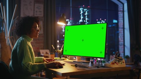 Latin Professional Female Freelancer Working on Desktop Computer with Green Chromakey Screen and Looking Attentively. Woman Scrolling With Computer Mouse while Finished her Project at Evening