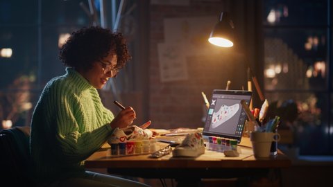 Creating Something Trendy. Black Woman Feel Inspired while Drawing at Evening. Female Designer Puts Patterns on Shoe Comparing with 3D Model on the Laptop Screen