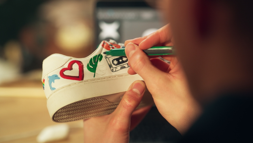 Male Artist Working on Colourful Design of Footwear in Loft Showroom. Fashion Designer Customising Pair of Shoes. Post Production Concept. Over the Shoulder Close-up