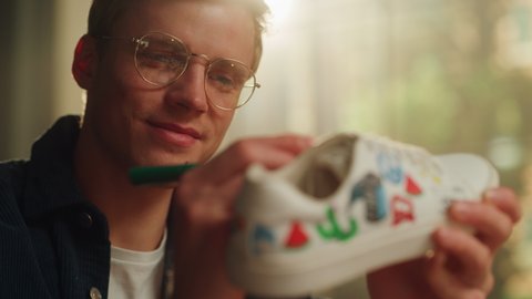 Close Up Portrait of Satisfied Male Artist Refreshing Sneakers by Painting on it at his Loft Flat. Creative Man Making Custom Made Design Shoes. Millennial People Concept