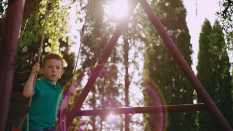 The boy rides on a children's swing. Happy child has fun and smiles while riding on a swing. Lifestyle video of a child who is happy. 