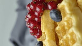 spinning Belgian waffles garnished with berries and soaked in maple syrup. food video. Delicious dessert.vertical screen