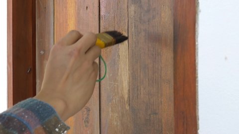Hand of a painter holding a painting plot is working to paint the wood.