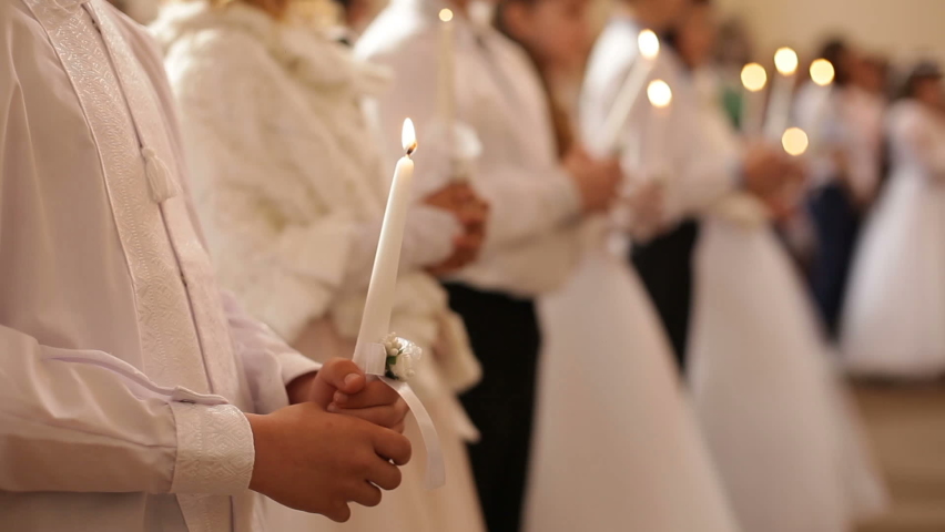 Children stand in the church at the first communion and hold lit candles in their hands. Christian traditions, children receive the Eucharist.
 Royalty-Free Stock Footage #1090539973
