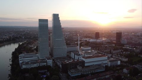 Basel, Switzerland - 19. May 2022: Aerial panorama of Basel city orbiting the Roche Headquarters at during sunset. Airplane passing by in the background.