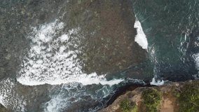 Shooting the ocean from a height with a drone. Top view of the large turquoise waves of the Indian Ocean. White foam from the waves and clear water with a rocky bottom. Video from the trip.