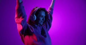 Disco dance. One smiling young girl listening to music in headphones and dancing on purple background in neon light, filter. 4K. Concept of emotions, youth, sales and aspiration. Looks happy