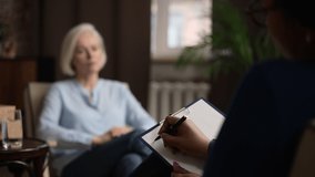 Close view of psychologist is writing and female patient speaking during consultation . 4k African American woman writes on clip board and listens to story, elderly person speaks and sits on