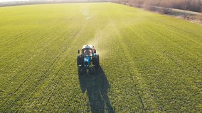 Drone footage tractor spreading artificial fertilizers in green field. Farming tractor spraying on field with herbicides. Industrial machine fertilizing a field.Chemicals used by agricultural tractor.
