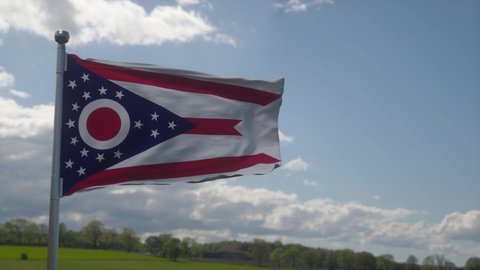 Ohio flag on a flagpole waving in the wind, blue sky background