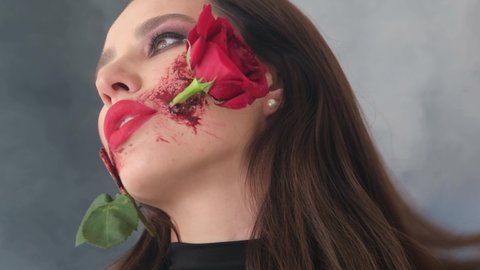 Portrait of a girl holding a red rose in her mouth. Makeup for Halloween, rose flower in mouth.