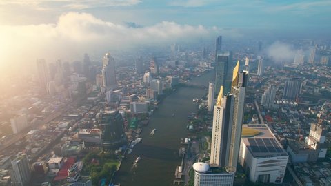 BANGKOK THAILAND - 2022 March 27, 4K : Drones fly over the Chao Phraya River, buildings and business districts in Bangkok. Amazing sunrise drone footage. Aerial top cityscape view from drone
