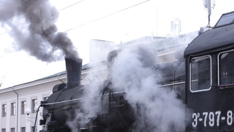 Steam locomotive train approaching station passing through goods yard leaking smoke and steam ignited from behind, creating an atmospheric.