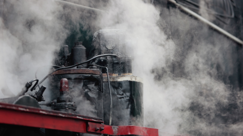 Vintage steam train locomotive. Pair locomotive train leaking smoke, steam ignited from behind. Antiquarian black steam engine. Old vintage train on the railroad. Close-up