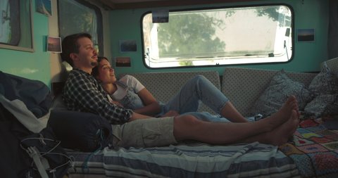 Cinematic shot of carefree couple in love having fun to speak to each other relaxed inside their trailer while enjoying together romantic trip with camping caravan.