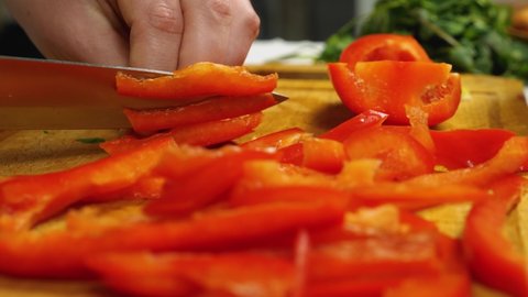 In slow motion, the cook is slicing red bell peppers on the cutting board. Close-up. Vegetarian Cuisine. The concept of delicious and healthy food. Selective focus