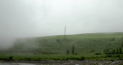 Stratus clouds covering green mountain hill with high voltage lines during rainy day