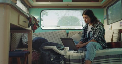 Cinematic shot of young woman is using laptop for work or study online inside trailer during family trip with rv camping caravan.