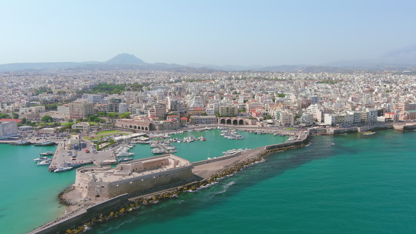 Heraklion, Greece: Aerial view of capital city of Greek island of Crete, Rocca a Mare Fortress, clear waters of Mediterranean Sea, yachts and ships in city marina - landscape panorama of Europe from a Royalty-Free Stock Footage #1090562347