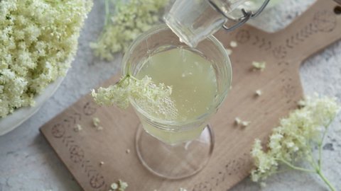 Pouring elder flower syrup into a glass decorated with fresh blossoms