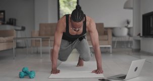 African American male practicing fitnes at home interior. Healhy workout living lifestyle concept using laptop and other modern technology for online training