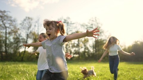 Children play in spring vacation park.Active happy group of kid run with a dog on grass in field in summer.Family in nature with pet.Child on play.Happy family concept.School in garden with dog