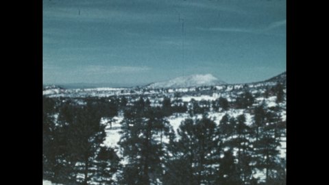 1980s: Snow covers the ground on a high plain dotted with clumps of trees. Two men on horses ride through the snow. Rifles on their saddles. Cougar watches from a ridge.