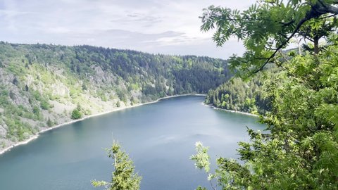 Aerial view of Lac Blanc in Alsace and its surrounding forests and hills, from the top of the mountain in spring on an overcast day