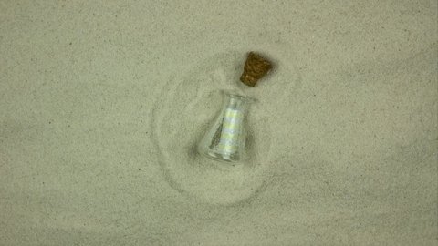 Corked transparent bottle in the sand. Blank letter from a bottle. Stop motion 