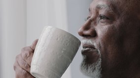 Side view african american old 60s lonely business man drinking coffee tea from cup mug looking out window thinking contemplating daydreaming relaxing enjoying fragrant drink in morning home office - Powered by Shutterstock - Get 15% off with code: PIKWIZARD15