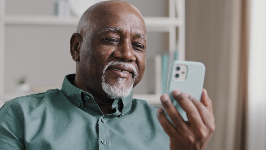 Senior elderly 60s businessman sitting on office couch has video call with mobile app. Old african american man holding smart phone calling online conference chat talking relaxing on sofa at home Royalty-Free Stock Footage #1090574165