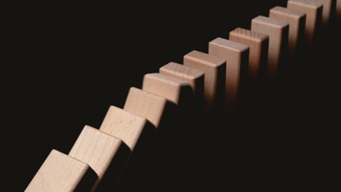 Row of wooden domino falling down against black background. Domino effect.