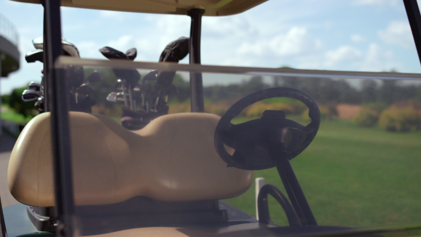 Golf cart equipment clubs at green course. Empty driving car stop at country club close up. Drive seat windshield wheel in buggy design. Sport equipment accessories on golfing fairway. Luxury concept.