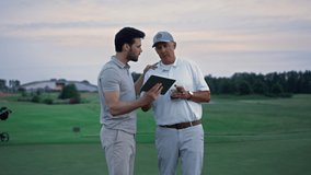 Modern sportsmen holding tablet browsing web on golf field. Two players looking digital device screen tab searching internet at country club landscape. Online communication activity nature concept.