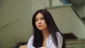 A beautiful Asian woman is thinking on the stairs. Close-up