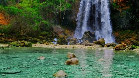 Beautiful large waterfall in a real time. Rocks, stones, green trees and bushes. Horizontal video. Turquoise water color.  