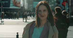 Beautiful thoughtful happy relaxed European woman in autumn coat smiling at camera outside in autumn city slow motion.